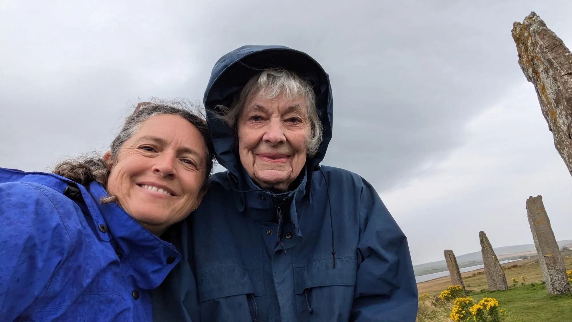 Kim and Dee in hooded rain jackets beside ancient standing stones
